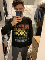 A man takes a mirror selfie in a closet wearing a black long-sleeve crewneck sweatshirt with a colorful Christmas-themed graphic that reads 'GAY APPAREL'.