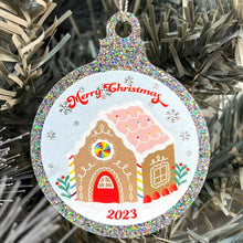 Load image into Gallery viewer, Close up of a white Christmas tree displaying a silver glitter bauble featuring a classic gingerbread house illustration with rainbow accents. Text reads Merry Christmas at the top and 2023 at the bottom.