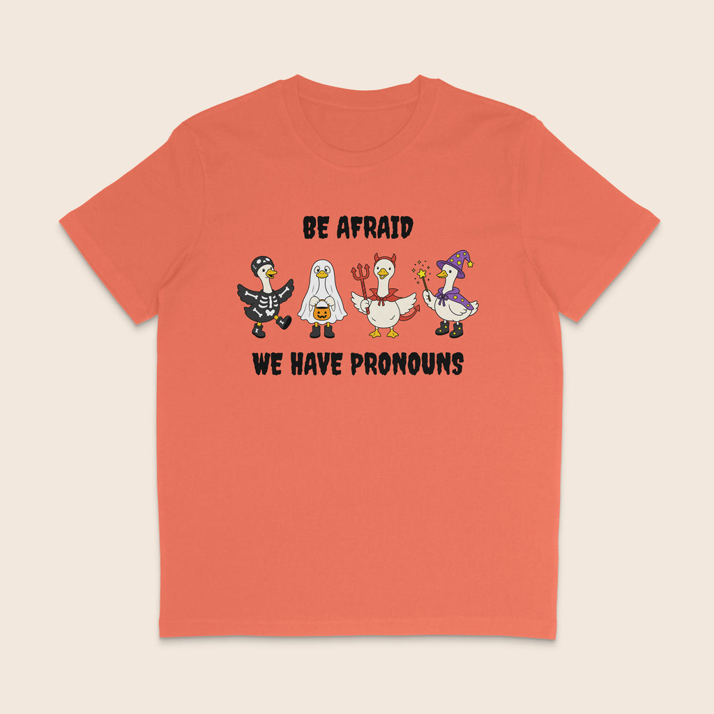 Orange Fiesta T-shirt with four geese dressed in Halloween costumes and the words Be Afraid We Have Pronouns.