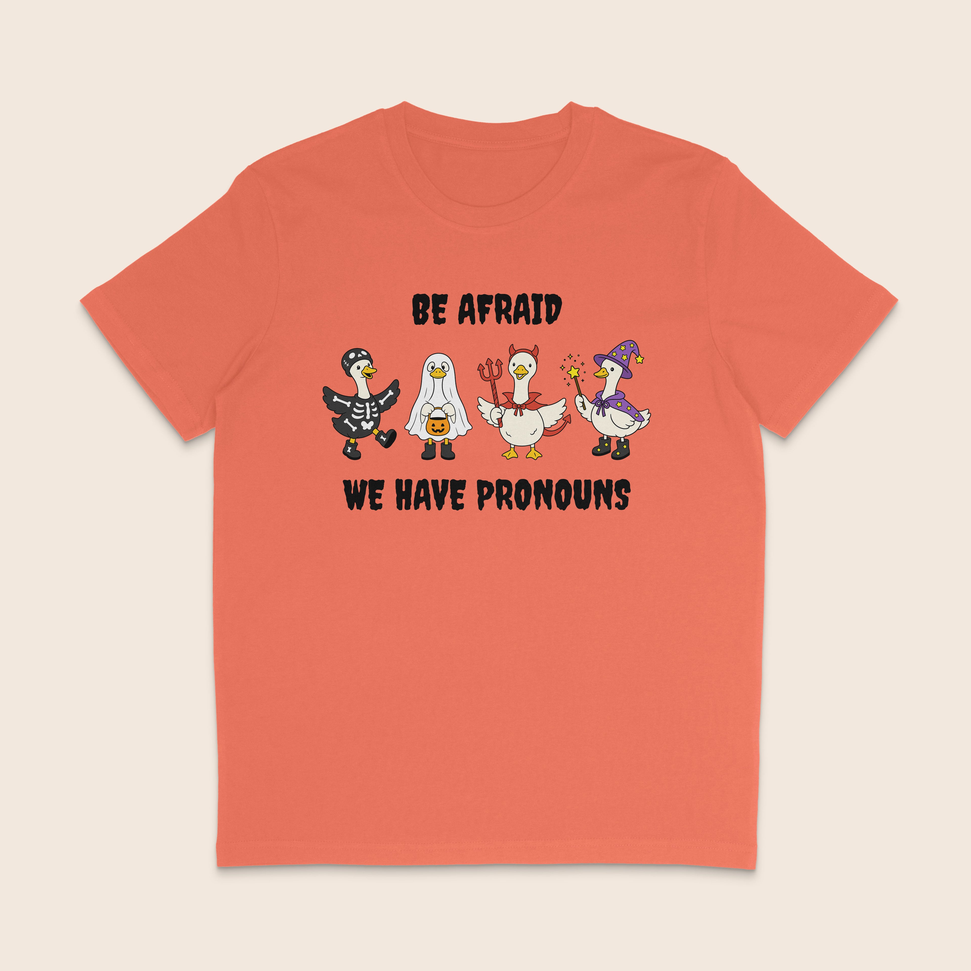 Orange Fiesta T-shirt with four geese dressed in Halloween costumes and the words Be Afraid We Have Pronouns.