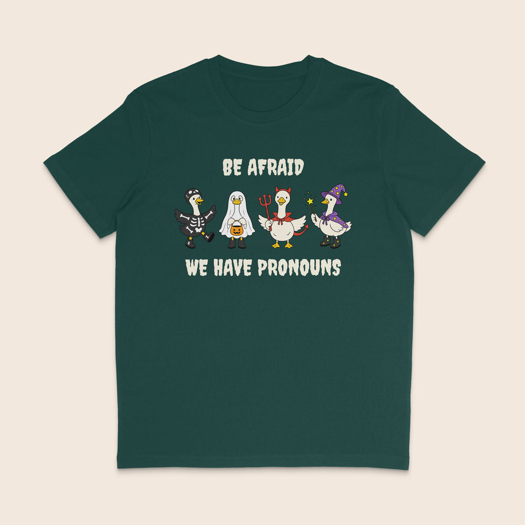 Glazed green T-shirt with four geese dressed in Halloween costumes and the words Be Afraid We Have Pronouns.