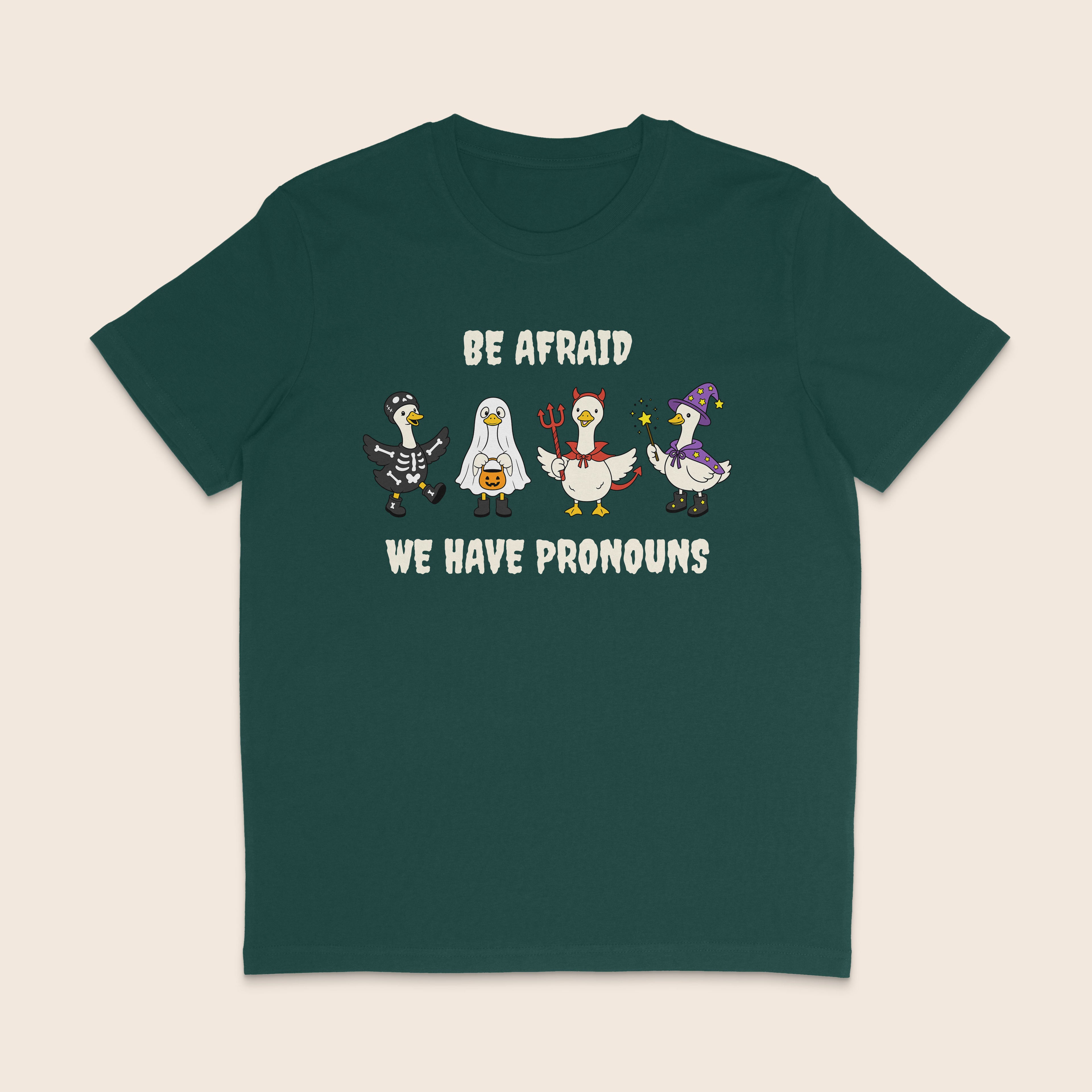 Glazed green T-shirt with four geese dressed in Halloween costumes and the words Be Afraid We Have Pronouns.