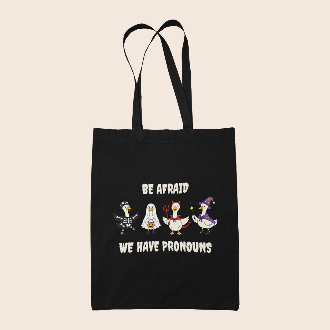 Black cotton tote bag featuring four geese in Halloween costumes with the words Be Afraid We Have Pronouns