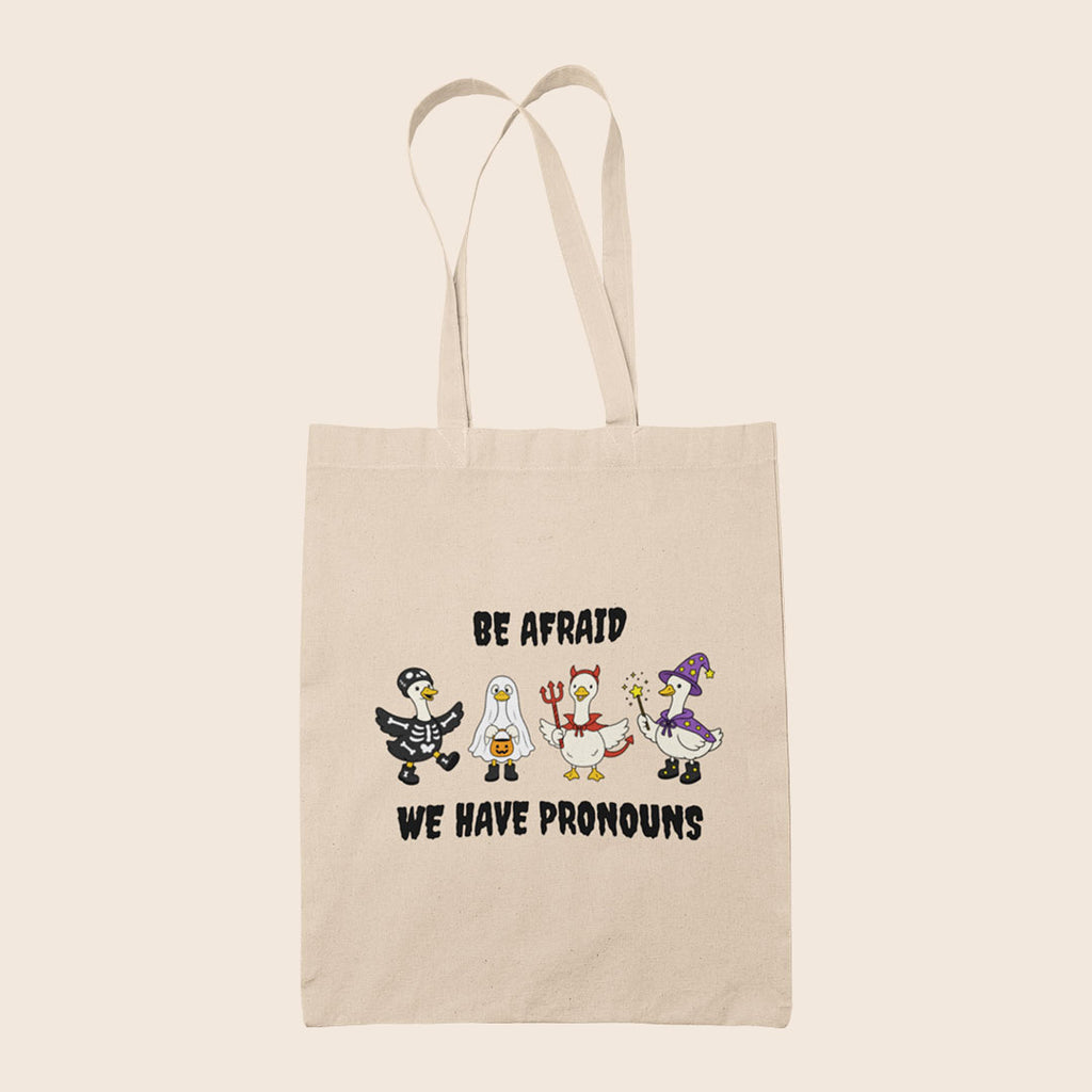 Natural cotton tote bag featuring four geese in Halloween costumes with the words Be Afraid We Have Pronouns