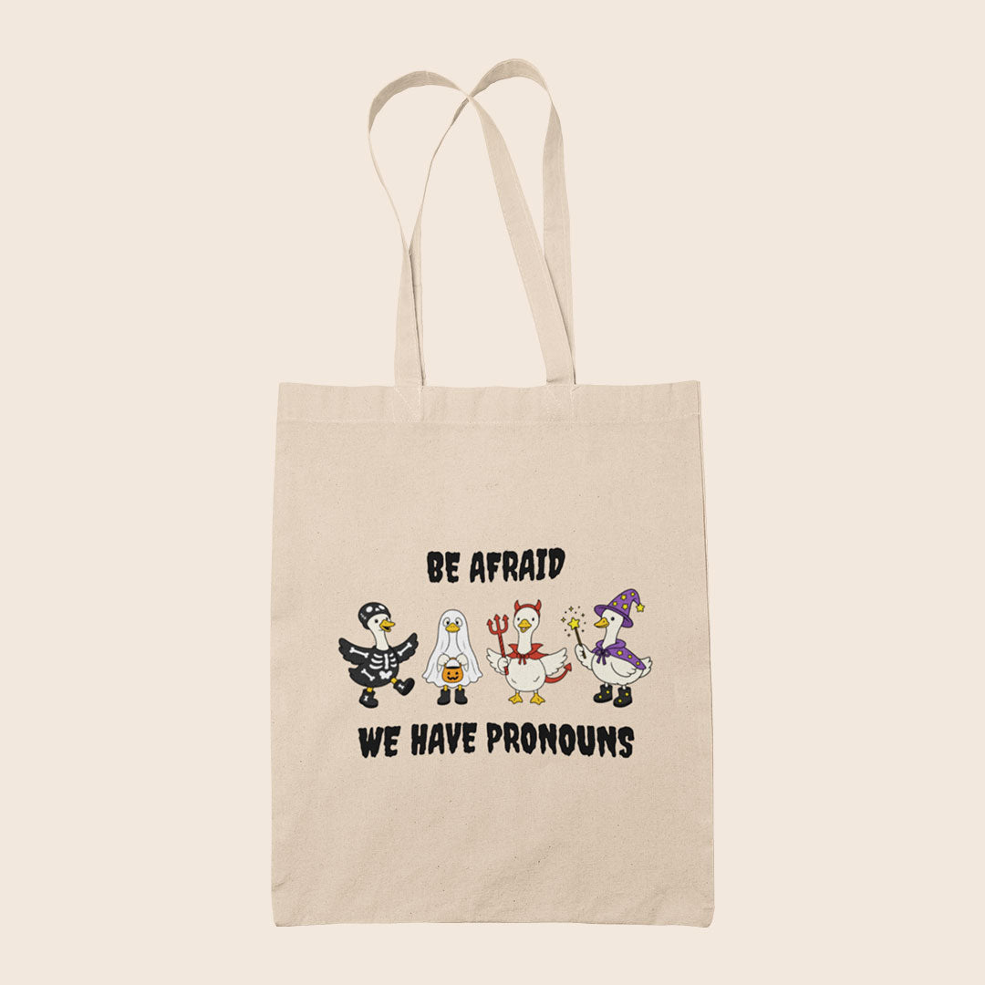 Natural cotton tote bag featuring four geese in Halloween costumes with the words Be Afraid We Have Pronouns