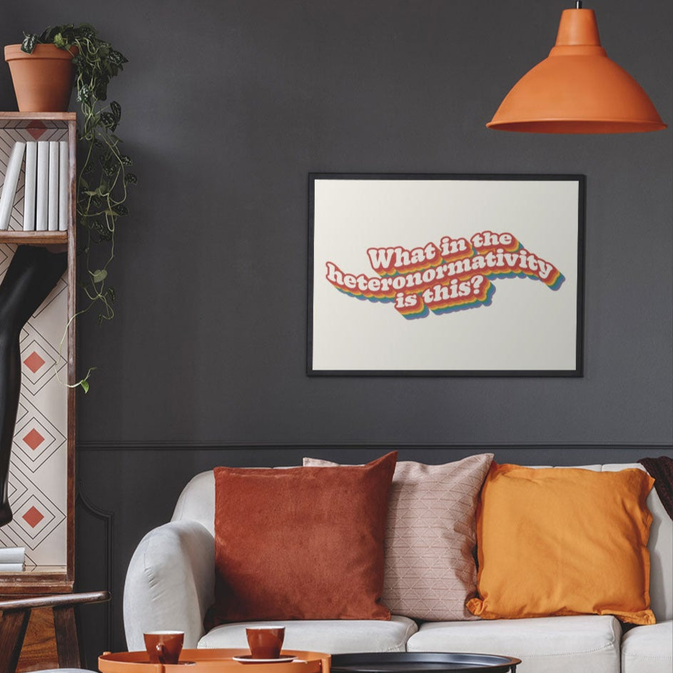 A modern living room with dark walls and warm-toned decor, featuring a What in the heteronormativity is this? print framed and hung above a sofa.