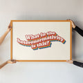 Two people holding up a large framed What in the heteronormativity is this? print, showcasing its bold typography and vibrant rainbow accents.