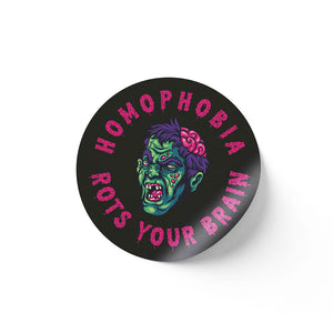 A round black sticker with a vibrant illustration of a green-skinned zombie head with a partially exposed brain, surrounded by the text "HOMOPHOBIA ROTS YOUR BRAIN" in pink, dripping letters.