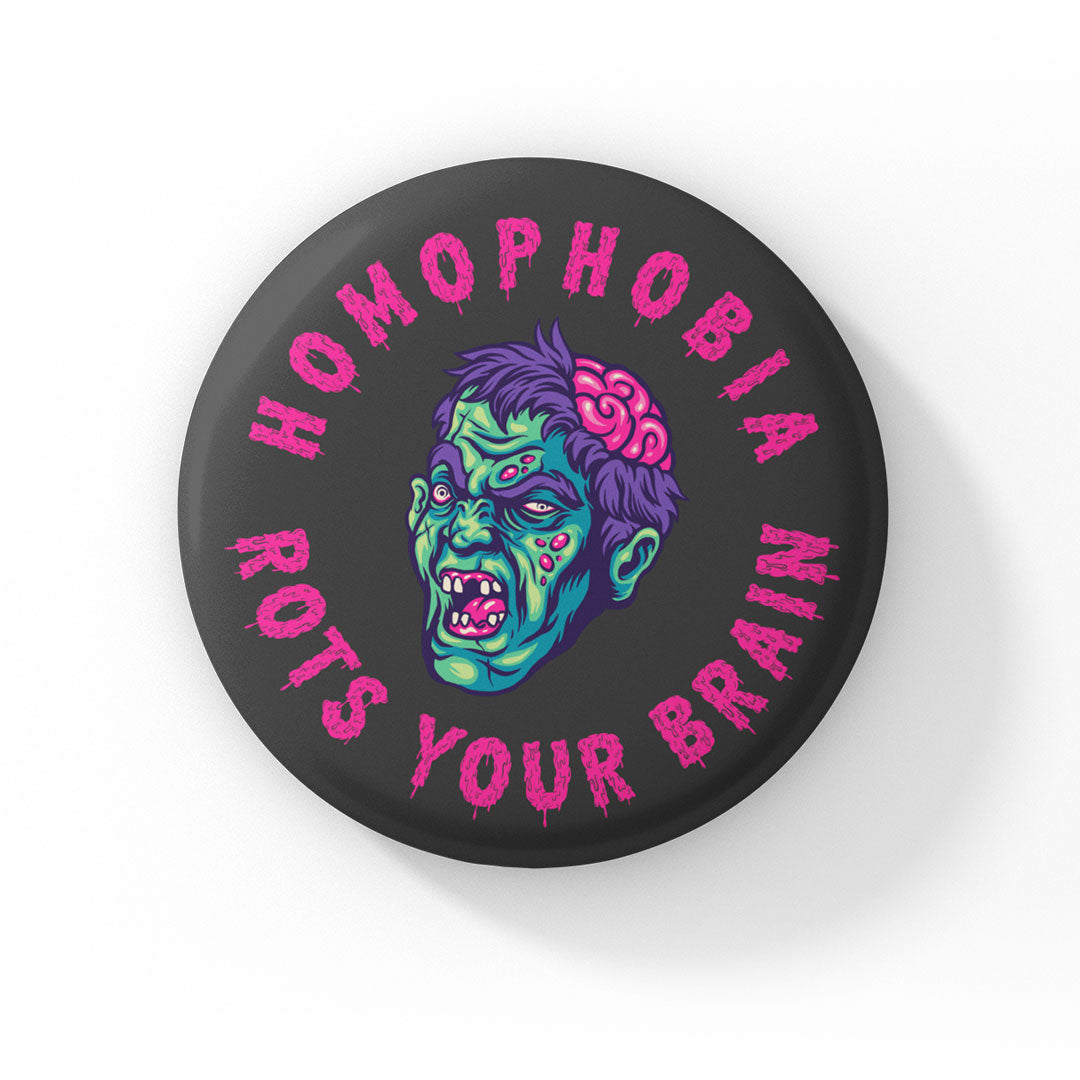 A round badge with a black background featuring a cartoon zombie head with green skin, purple hair, and exposed brain. The text "HOMOPHOBIA ROTS YOUR BRAIN" is written in bold, dripping pink letters around the zombie head.