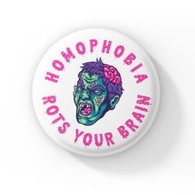 Load image into Gallery viewer, A round badge with a white background displaying a cartoon zombie head with green skin, purple hair, and exposed brain. The text &quot;HOMOPHOBIA ROTS YOUR BRAIN&quot; is written in bold, dripping pink letters encircling the zombie head.