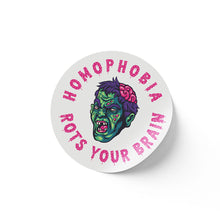 Load image into Gallery viewer, A round white sticker featuring a vivid illustration of a green-skinned zombie head with a partially exposed brain. The text &quot;HOMOPHOBIA ROTS YOUR BRAIN&quot; is written around the illustration in bold pink, dripping letters.