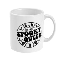 Load image into Gallery viewer, The right side of a white ceramic mug showcasing a large, black graphic that reads &quot;In My Spooky Queer Era Est. 1692.&quot; The design is framed by small bats and skulls, adding a quirky and gothic element.