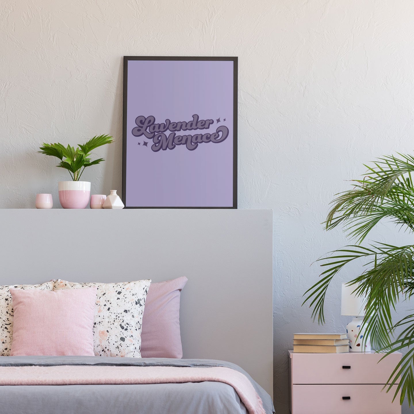 A framed Lavender Menace print in a modern bedroom setting. The purple-toned artwork is mounted on a light grey wall above a bed with soft pastel bedding and pink accents.