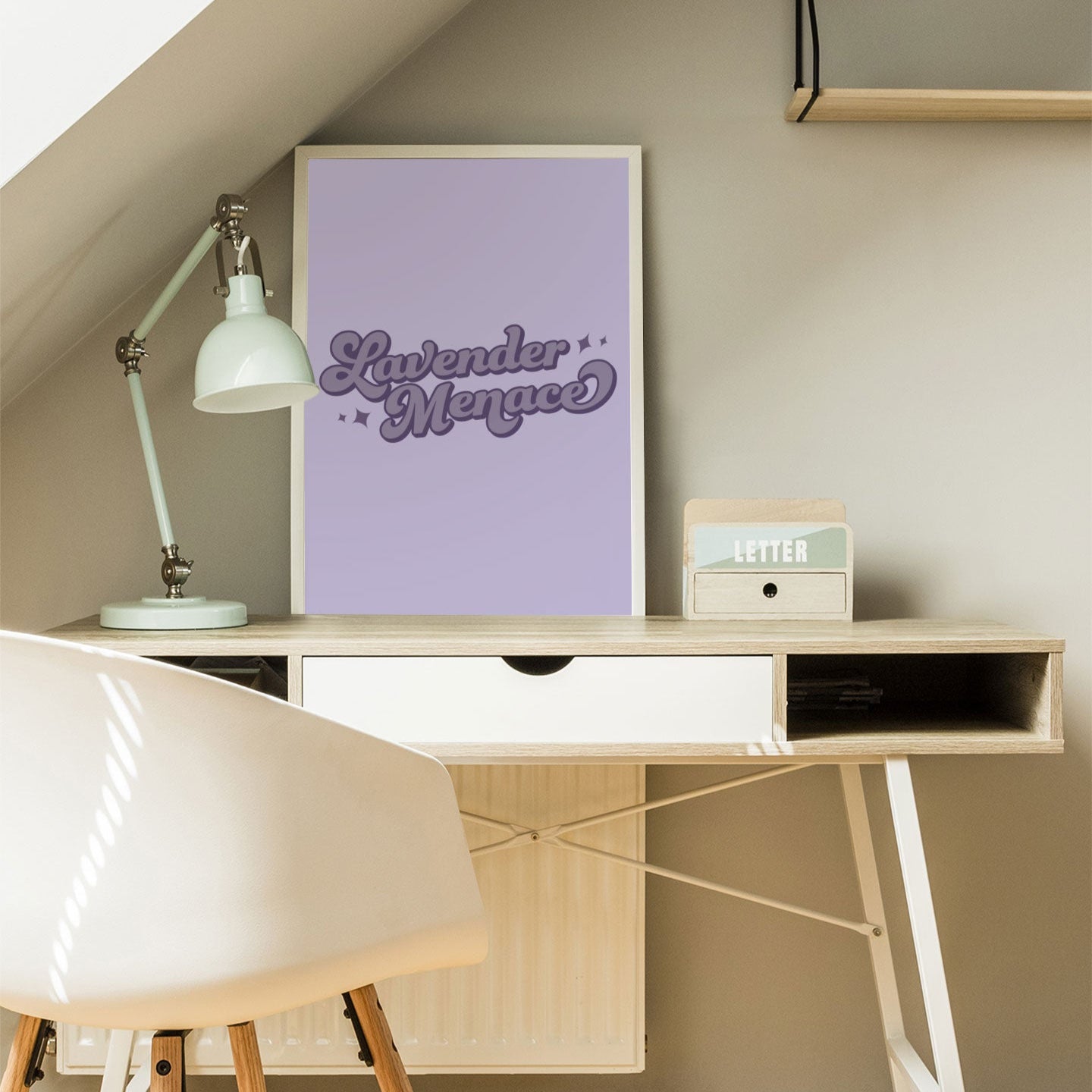 A Lavender Menace print on a minimalist desk. The lavender-hued typography print is framed in white, adding a pop of queer history to a bright and neutral workspace.