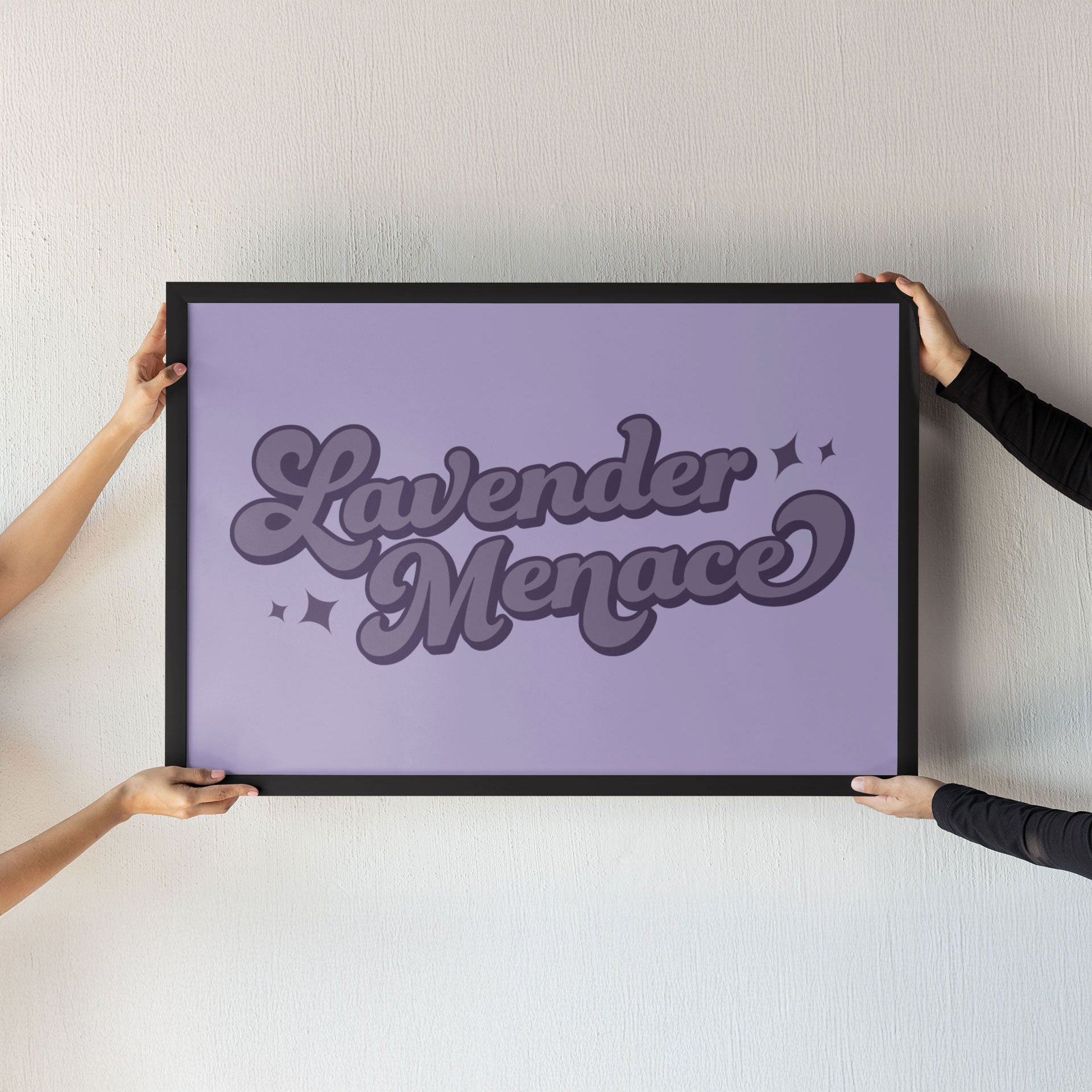 Two hands holding a large framed Lavender Menace print against a neutral wall. The bold purple text design is a powerful nod to LGBTQ+ activism.