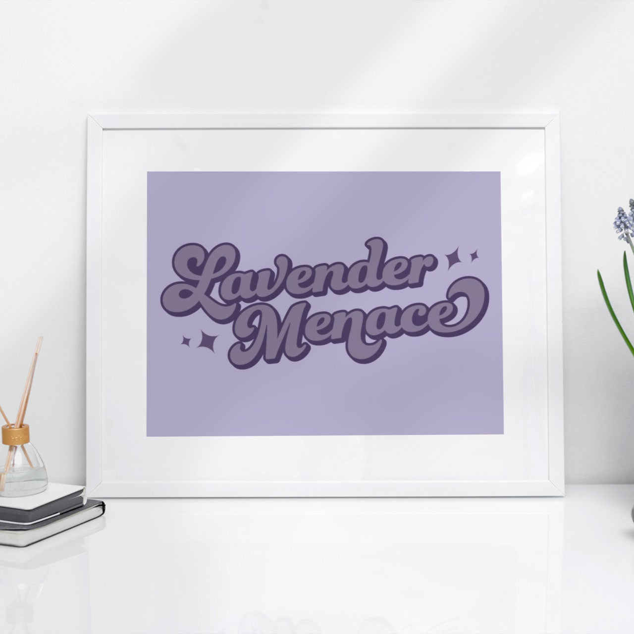 A framed Lavender Menace print styled on a sleek white desk. The subtle lavender tones and vintage-inspired typography bring a touch of LGBTQ+ pride to any space.