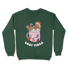 Load image into Gallery viewer, Bottle Green sweatshirt featuring retro text reading &#39;cosy vibes&#39;. The image shows a mug of hot chocolate with marshmallows and a gingerbread man wearing a Santa hat. A candy cane in the mug and lights around the mug are the colours of the lesbian pride flag.