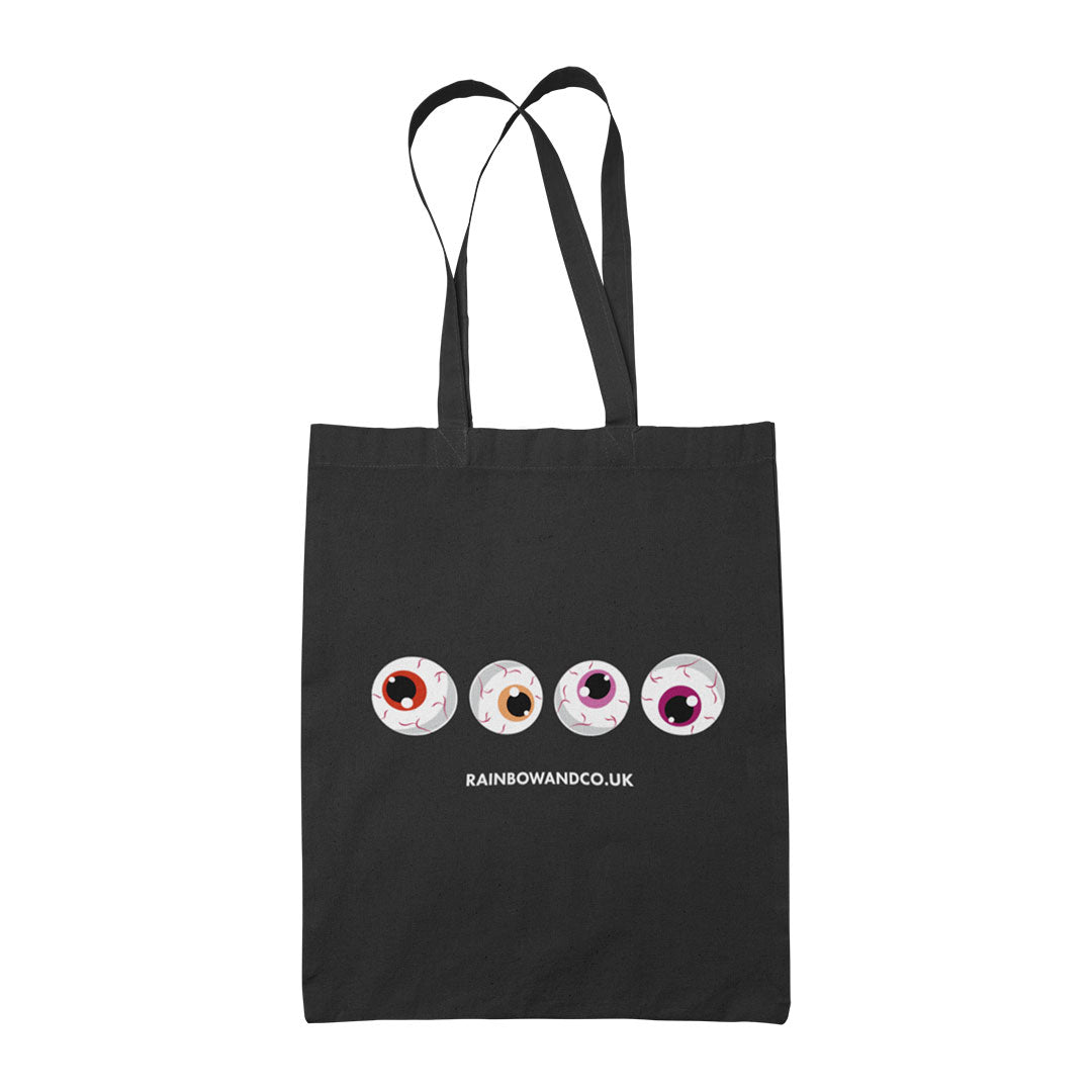 A black tote bag with four cartoonish eyeballs aligned in a row. The colours of the eyeballs include red, orange, and pink. The bottom of the design features the text "RAINBOWANDCO.UK".
