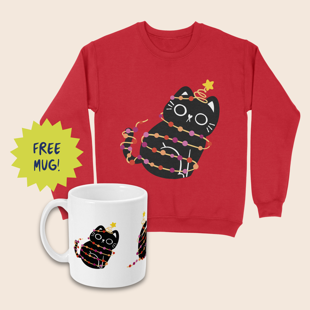 Red Christmas jumper and white mug featuring black cats wrapped in orange and pink fairy lights with yellow stars. The mug sits in front of the jumper on a cream background, beside a lime-green starburst reading “FREE MUG!”
