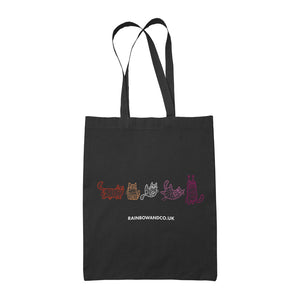 A black tote bag showcasing five mummy cats in various colours representing the lesbian pride flag: orange, white, pink, and magenta. Each cat has a unique pose and expression. The text "rainbowandco.uk" is placed beneath the design.