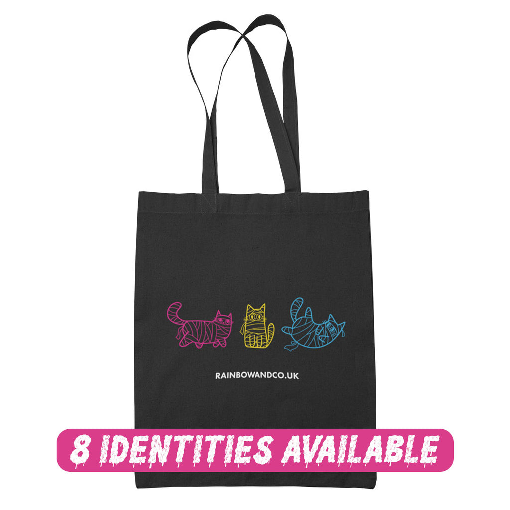 A black tote bag with three mummy cats in different pride colours: pink, yellow, and blue. The bottom of the bag reads "rainbowandco.uk," and a banner across the bottom says "8 Identities Available" in pink lettering.