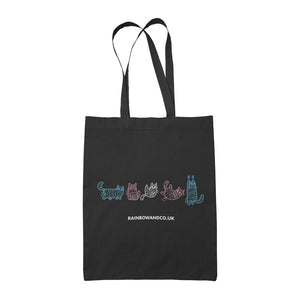 A black tote bag featuring five mummy cats in colours representing the transgender pride flag: light blue, pink, and white. Each cat is depicted in a playful manner. The text "rainbowandco.uk" appears beneath the design.