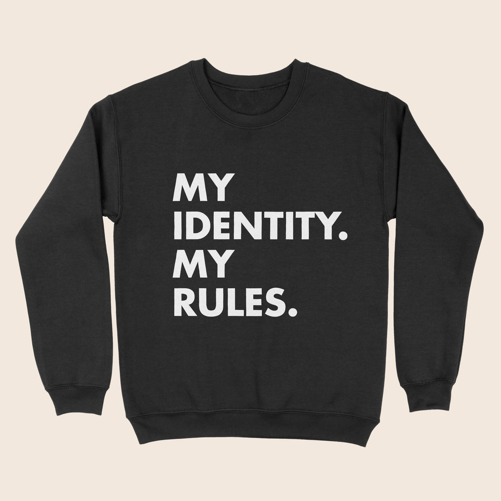 A black crewneck sweatshirt with bold white text printed in all caps reading “MY IDENTITY. MY RULES.” displayed against a neutral beige background.