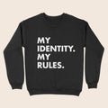 A black crewneck sweatshirt with bold white text printed in all caps reading “MY IDENTITY. MY RULES.” displayed against a neutral beige background.