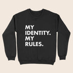 A black crewneck sweatshirt with bold white text printed in all caps reading “MY IDENTITY. MY RULES.” displayed against a neutral beige background.