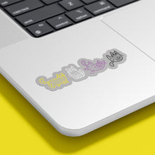 Load image into Gallery viewer, A laptop with stickers of mummy-wrapped cats in the colours of the non-binary flag. The cats are coloured in yellow, white, purple, and black.