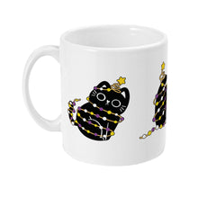 Load image into Gallery viewer, The left side of the white mug displaying the same cute black cat adorned in non-binary pride flag colours as it sits wrapped in twinkling holiday lights.