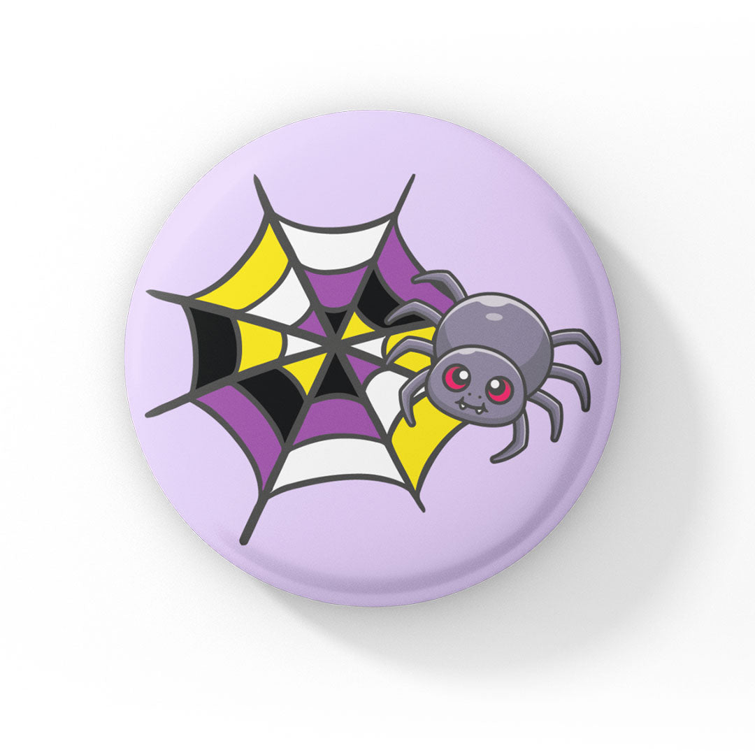 A circular badge with a grey spider with pink eyes on a web coloured in yellow, white, purple, and black, representing the non-binary pride flag. The badge has a pastel purple background.