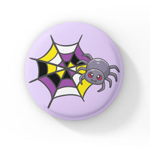 Load image into Gallery viewer, A circular badge with a grey spider with pink eyes on a web coloured in yellow, white, purple, and black, representing the non-binary pride flag. The badge has a pastel purple background.