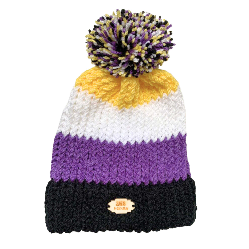 Striped knitted bobble hat in the colours of the Non Binary pride flag laying flat.