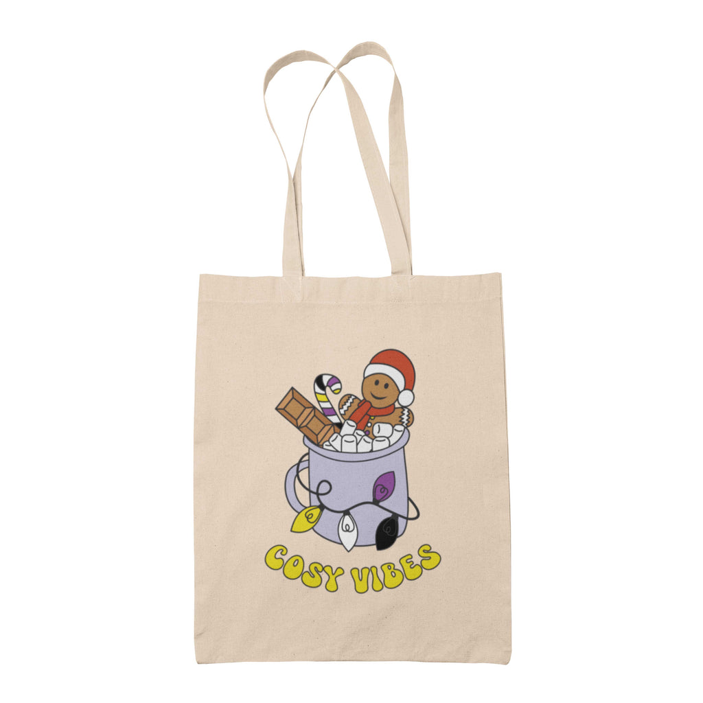 Natural tote bag featuring retro text reading 'cosy vibes'. The image shows a mug of hot chocolate with marshmallows and a gingerbread man wearing a Santa hat. A candy cane in the mug and lights around the mug are the colours of the non binary pride flag.