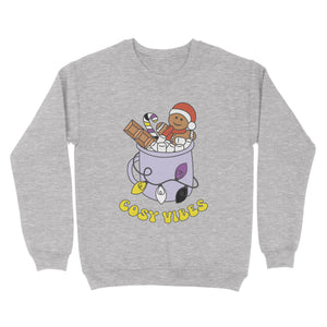 Heather Grey sweatshirt featuring retro text reading 'cosy vibes'. The image shows a mug of hot chocolate with marshmallows and a gingerbread man wearing a Santa hat. A candy cane in the mug and lights around the mug are the colours of the non binary pride flag.
