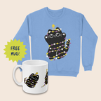 Light blue Christmas jumper and matching white mug featuring black cats wrapped in yellow, white and purple fairy lights, with yellow stars above their heads, arranged on a cream background. A lime-green starburst beside the mug reads “FREE MUG!”