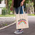 Natural cotton tote bag featuring the words “Pan & Perfect” with a rainbow arc in pansexual pride colours, worn over the shoulder outside