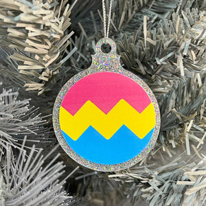 Close up of a white Christmas tree displaying a silver glitter bauble featuring a classic zig zag design in the colours of the pansexual pride flag.