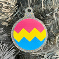 Close up of a white Christmas tree displaying a silver glitter bauble featuring a classic zig zag design in the colours of the pansexual pride flag.