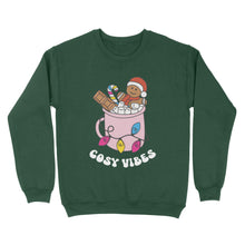 Load image into Gallery viewer, Bottle Green sweatshirt featuring retro text reading &#39;cosy vibes&#39;. The image shows a mug of hot chocolate with marshmallows and a gingerbread man wearing a Santa hat. A candy cane in the mug and lights around the mug are the colours of the pansexual pride flag.