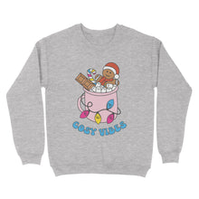Load image into Gallery viewer, Heather Grey sweatshirt featuring retro text reading &#39;cosy vibes&#39;. The image shows a mug of hot chocolate with marshmallows and a gingerbread man wearing a Santa hat. A candy cane in the mug and lights around the mug are the colours of the pansexual pride flag.