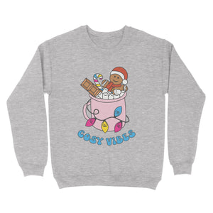 Heather Grey sweatshirt featuring retro text reading 'cosy vibes'. The image shows a mug of hot chocolate with marshmallows and a gingerbread man wearing a Santa hat. A candy cane in the mug and lights around the mug are the colours of the pansexual pride flag.