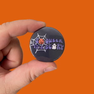 A black 38mm badge with text reading 'So Queer It's Scary' with images of a pumpkin, ghost, and spiders web
