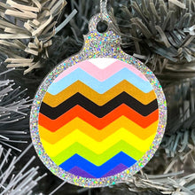 Load image into Gallery viewer, Close up of a white Christmas tree displaying a silver glitter bauble featuring a classic zig zag design in the colours of the progress pride flag.