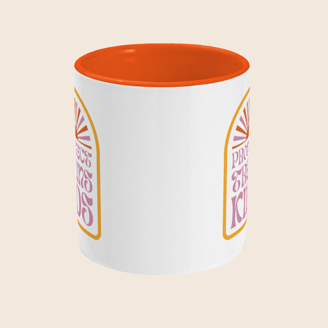 A white ceramic mug with a bright orange interior, featuring a retro-style graphic in the centre. The design shows a rising sun with rays above bold pink text reading "Protect Trans Kids" inside a rounded yellow border.