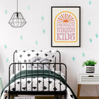 A framed Protect Trans Kids print hanging on the wall above a black metal bed with green and white bedding, surrounded by minimalist cactus wall decals.
