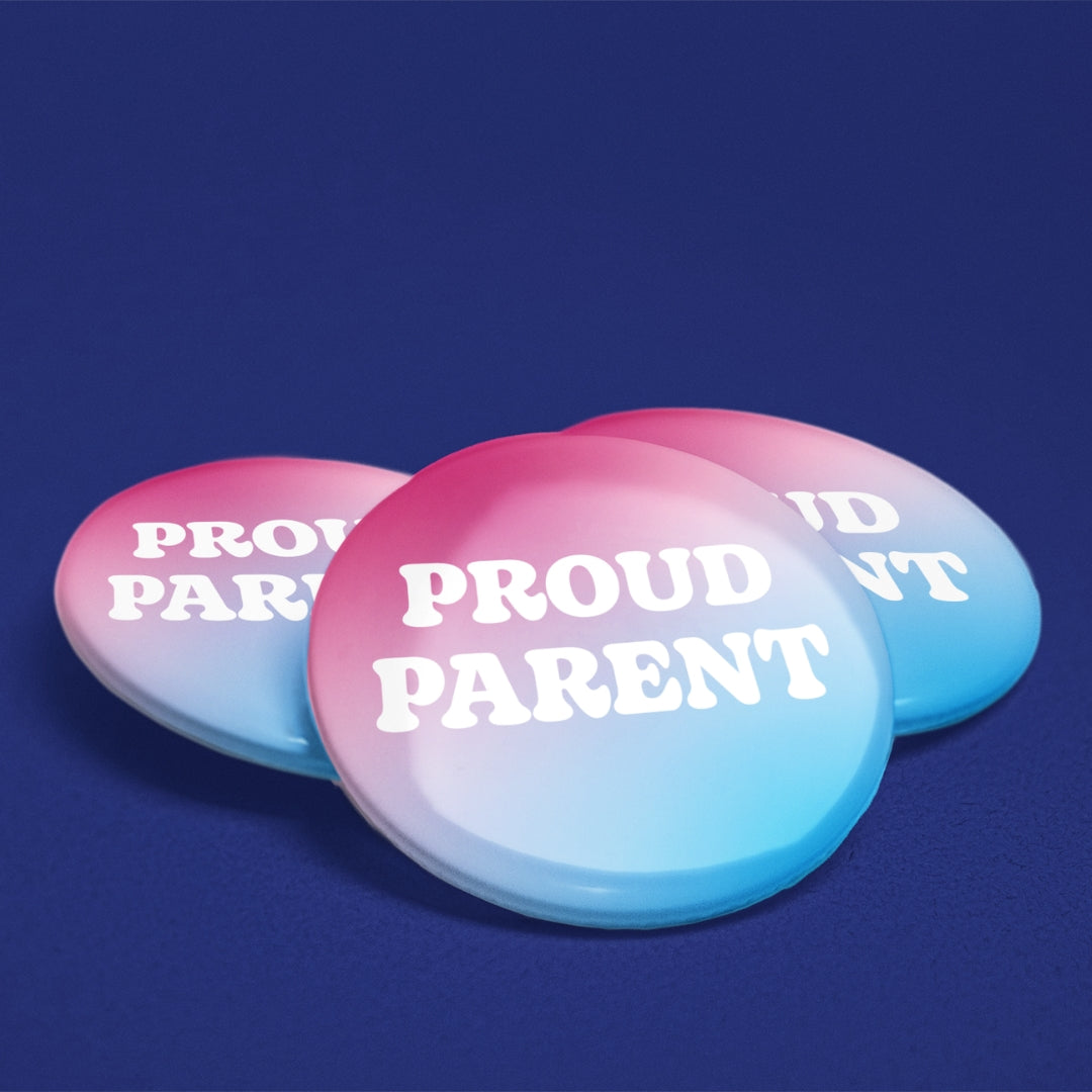 Three 38mm Proud Parent trans flag badges arranged on a blue background showing the glossy finish.