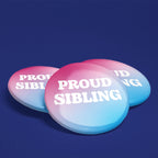 Three Proud Sibling transgender pride badges with pink, white and blue gradient background displayed on a dark blue surface.