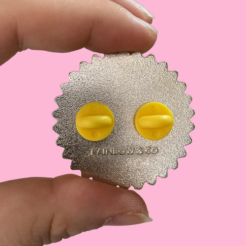 The back of a Queer Existence is Resistance Enamel Pin with two yellow rubber clutches